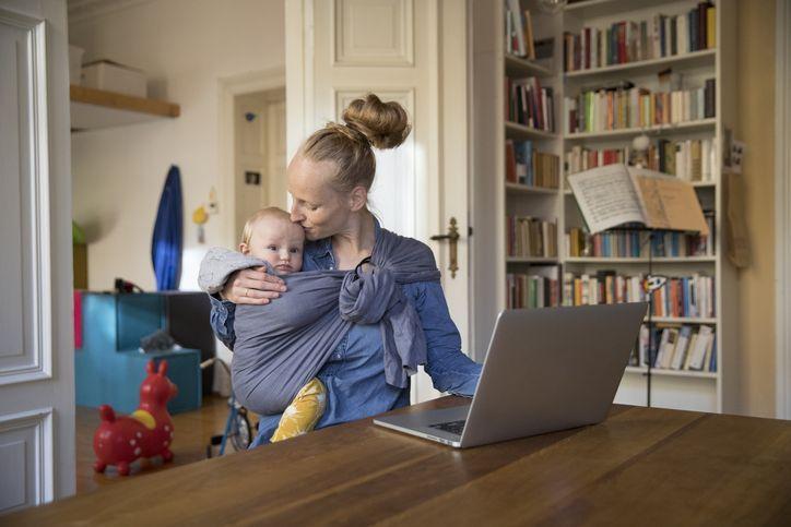 kobieta siedząca przed laptopem z dzieckiem w szarej chuście